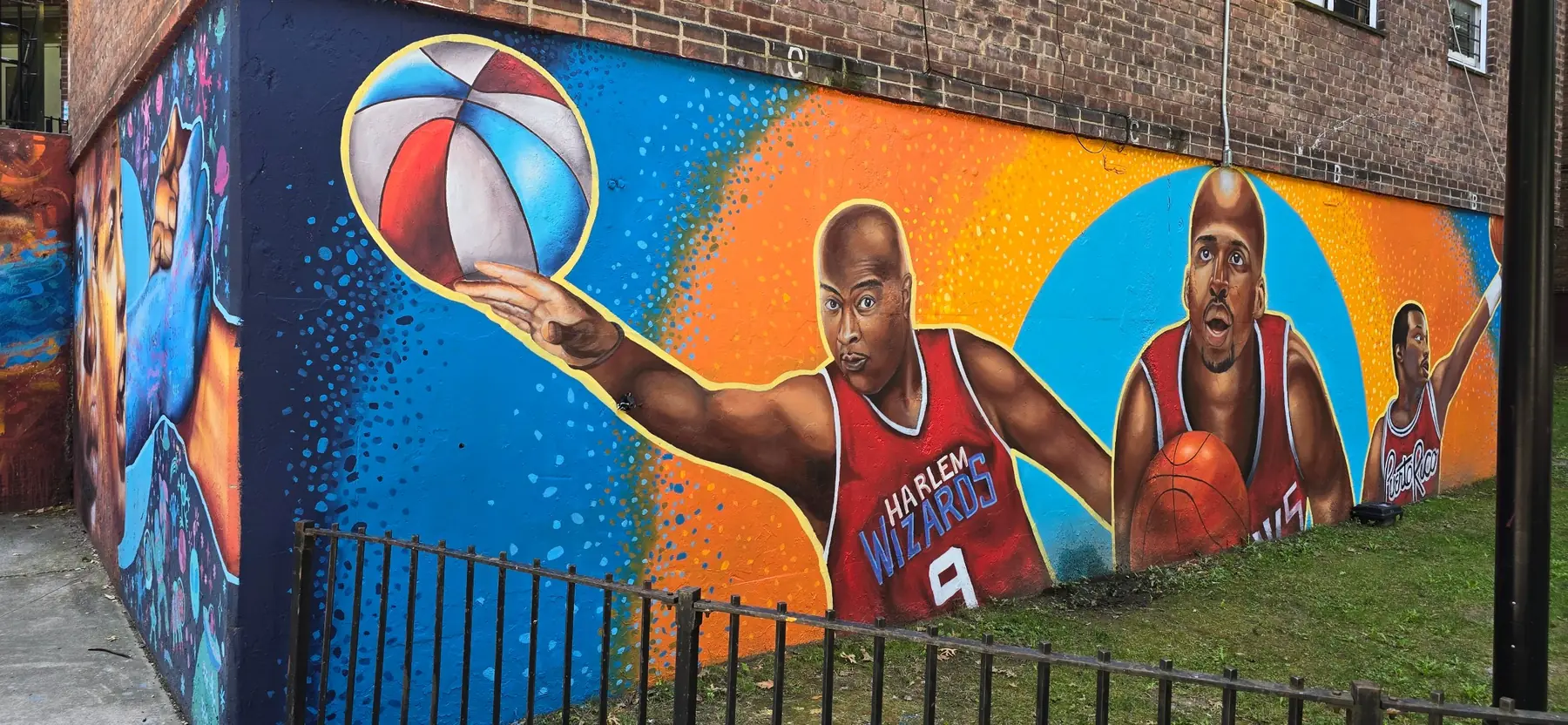 A long painted wall showing basketball players in red jerseys, one spinning a red, white and blue ball on a fingertip, against orange and blue