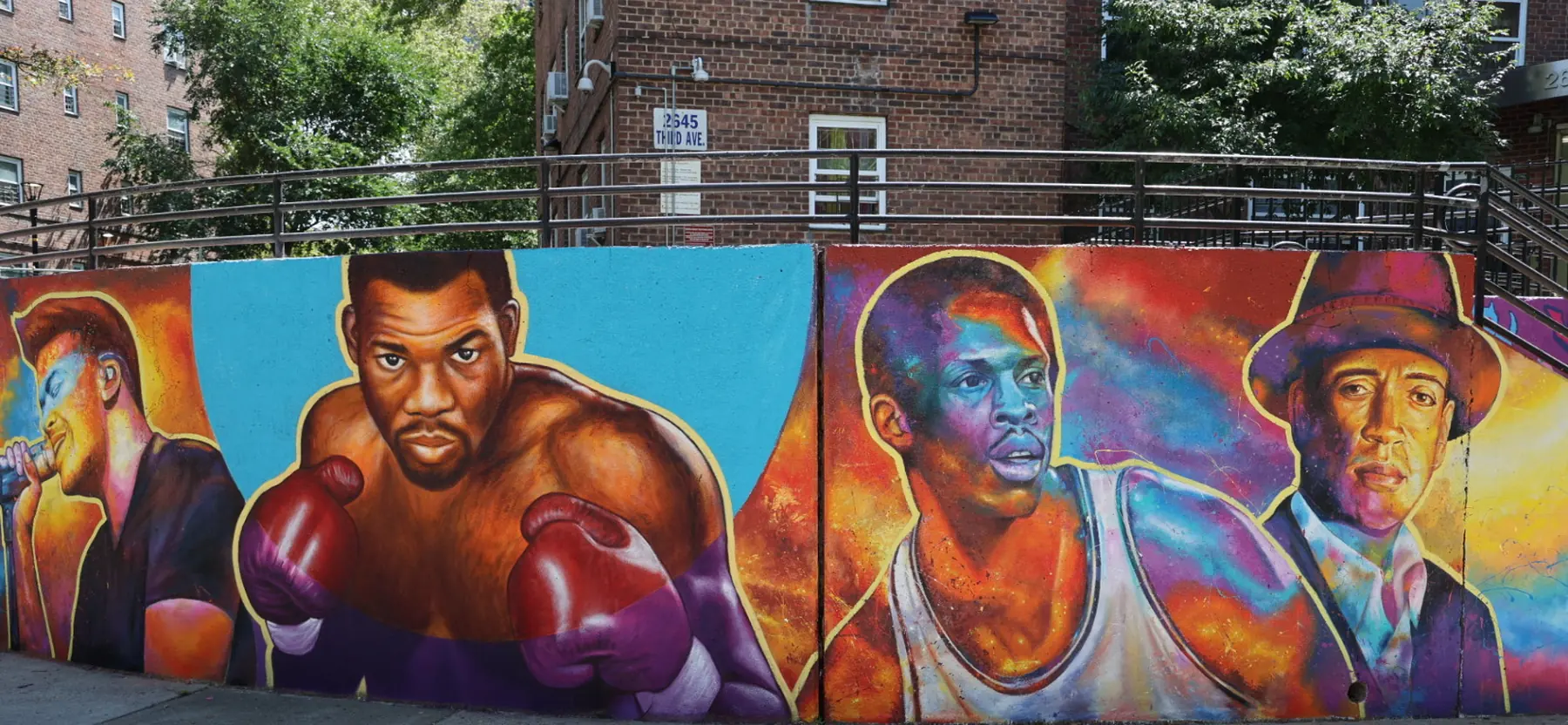 A painted wall at Patterson Houses showing a singer at a microphone, a boxer in red gloves, a basketball player in a white jersey and a man in a hat, each outlined in yellow against bright colour