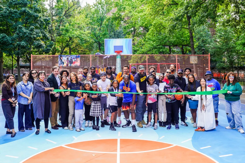 Residents, NYCHA staff and project partners holding a green ribbon across the newly opened basketball court at Patterson Houses